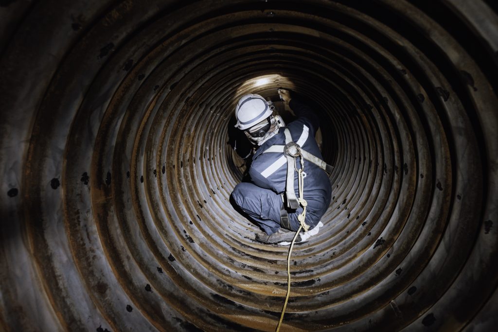 Trabalhador com EPI realiza inspeção dentro de espaço confinado conforme NR-33