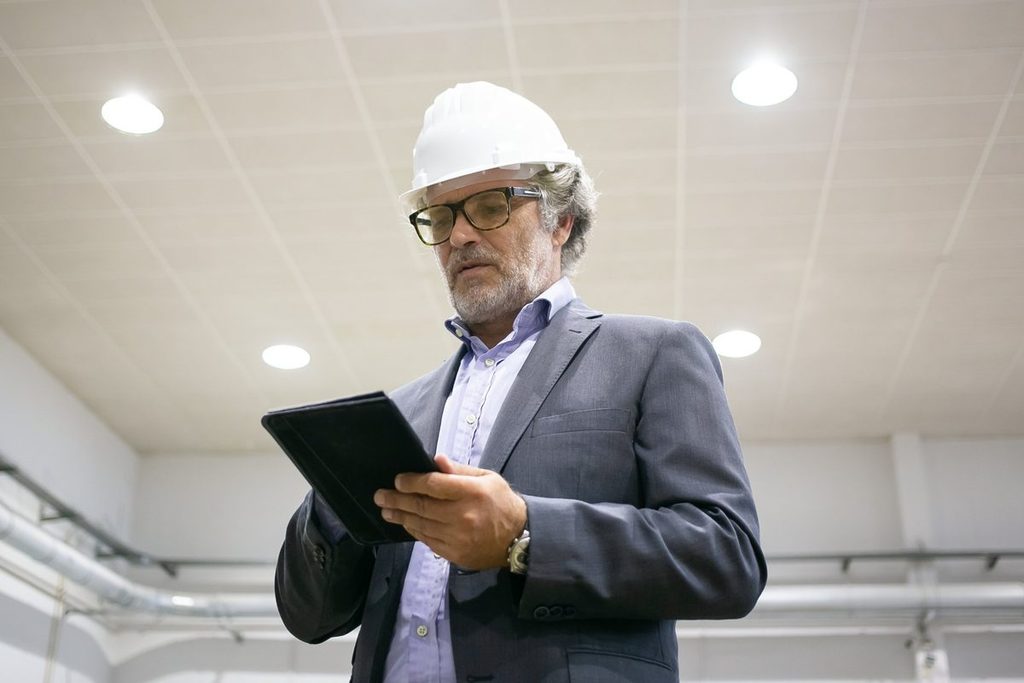 Gestor com capacete analisando a tributação de SST da empresa em um tablet dentro da indústria
